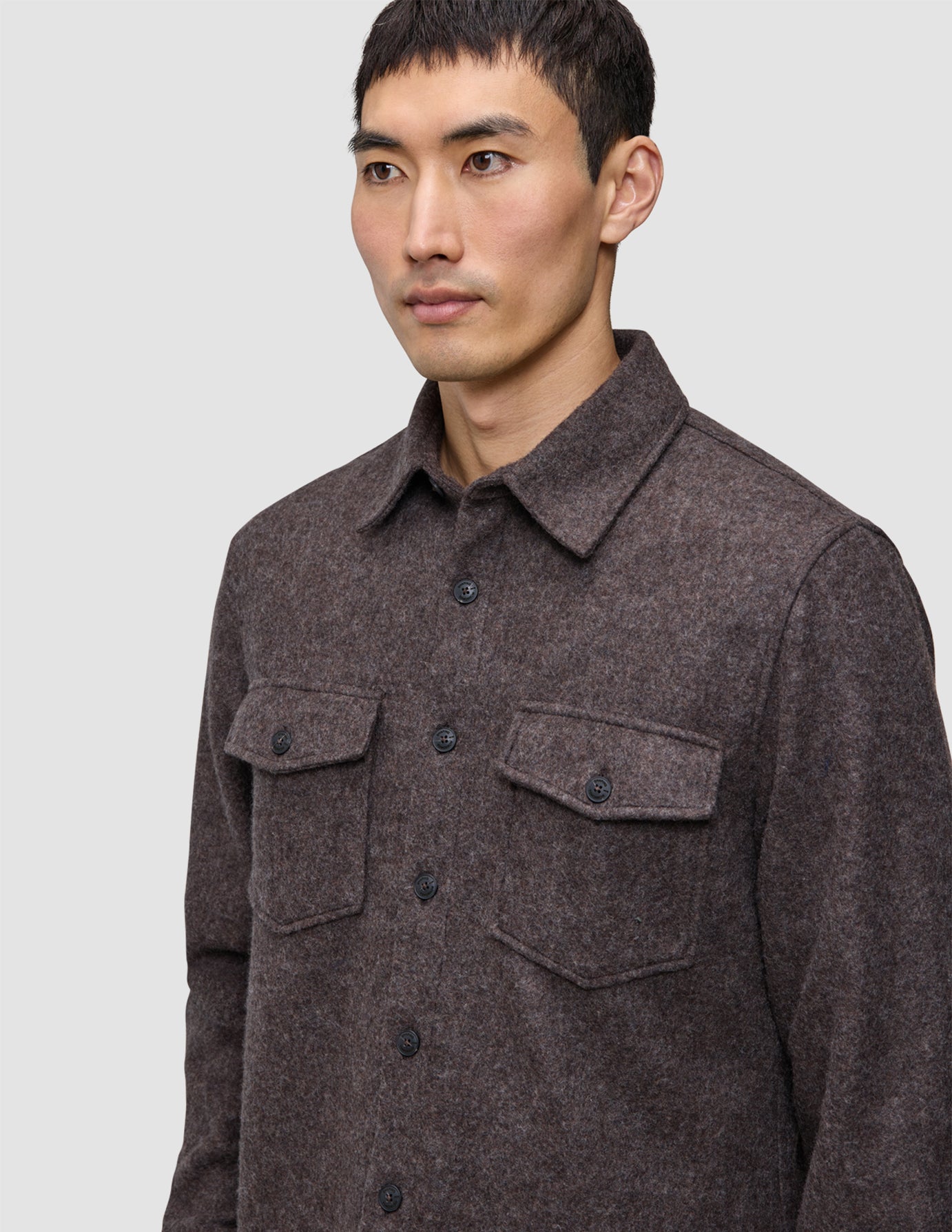 Ein Mann, der ein doppellagiges Woll-Overshirt in Sattelbraun trägt – ein braunes, doppellagiges Wollmodell mit zwei Brusttaschen, das im schlichten, skandinavischen Stil gefertigt ist.